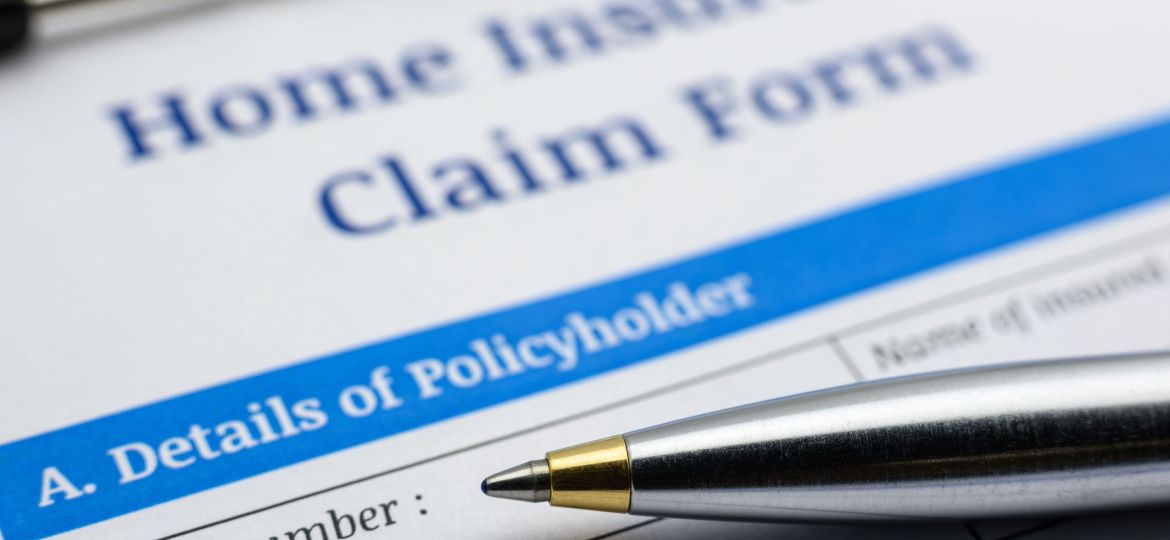 Blue ballpoint pen and a home insurance claim form on a clip board. A blank / empty form is waiting to be filled and signed by a policyholder / insured person.